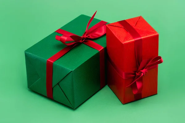 Two colorful present boxes with red ribbons and bows on green background — Stock Photo