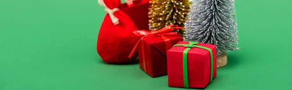 Encabezado del sitio web de plata decorativa y árboles de Navidad de oro cerca de cajas de regalo y saco en verde - foto de stock