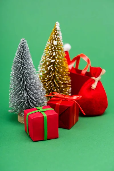 Silver and golden decorative christmas trees near gift boxes, sack and shopping bag with santa hat on green — Stock Photo