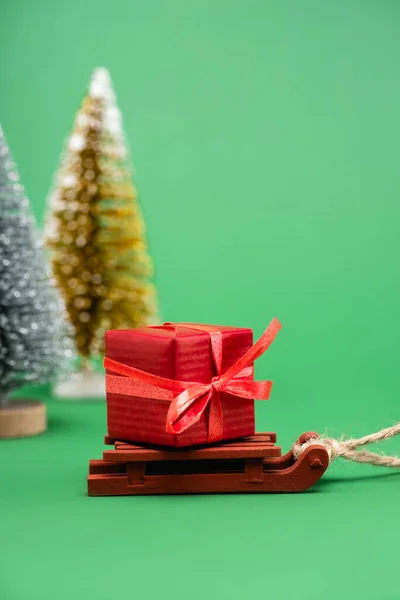 Вибірковий фокус срібних і золотих декоративних різдвяних ялин поблизу санки з подарунковою коробкою на зеленому — стокове фото