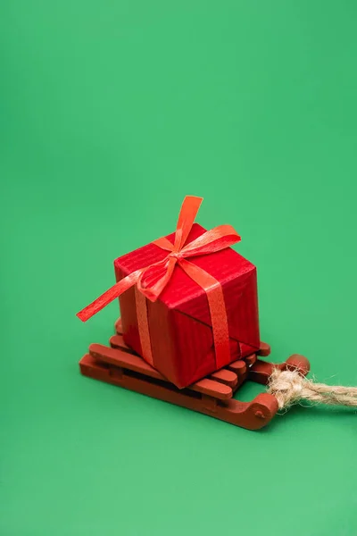 Scatola regalo rossa su slitta decorativa in legno su sfondo verde — Foto stock