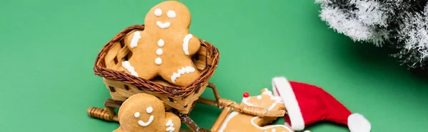 Horizontales Bild von Lebkuchenmännern und Hirschen in der Nähe von dekorativen Schlitten und Tannenzweig auf grünem Hintergrund — Stockfoto