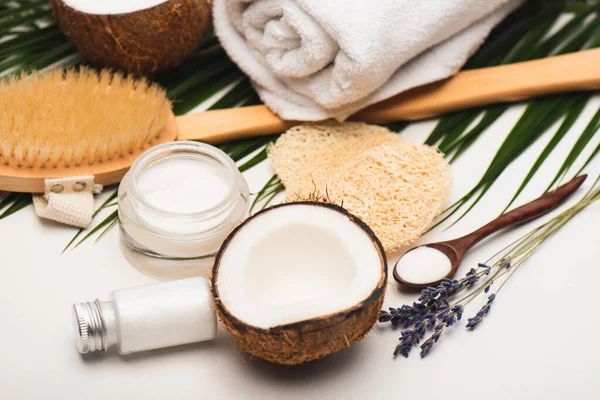 Moitié noix de coco, crème cosmétique, serviette de massage, éponges et feuilles de palmier sur surface blanche — Photo de stock