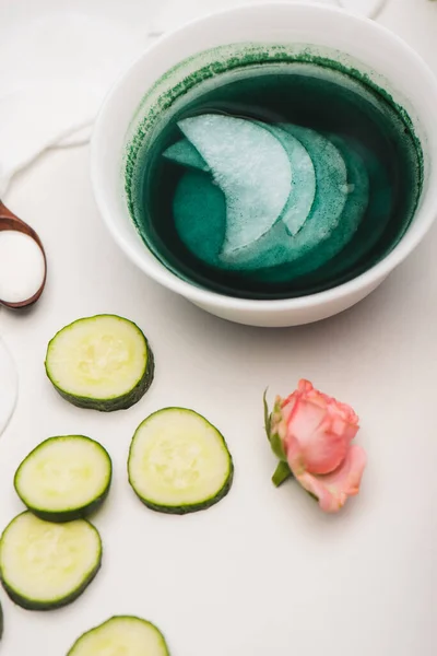 Rosa de té, rodajas de pepino, tazón con loción y almohadillas de algodón en la superficie blanca — Stock Photo