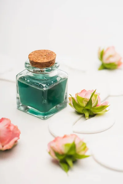 Bottiglia di tonico verde vicino a rose da tè e batuffoli di cotone su sfondo bianco sfocato — Foto stock