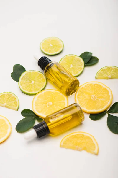 Juicy lemon and lime slices near bottles with citrus essential oil and rose leaves on white — Stock Photo