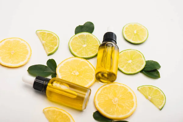 Bottles with citrus essence, fresh lemon and lime slices near rose leaves on white surface — Stock Photo