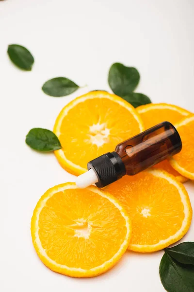 Foco seletivo de garrafa com óleo essencial cítrico perto de fatias de laranja e folhas de rosa no branco — Fotografia de Stock