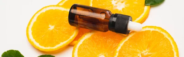 Rodajas de naranja con botella de esencia de cítricos en la superficie blanca, bandera - foto de stock