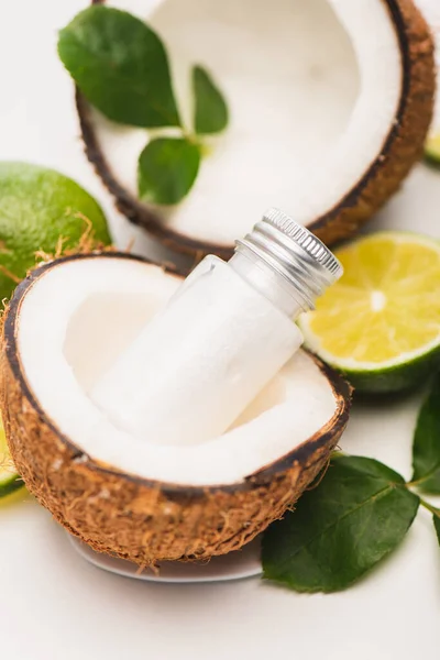 Flasche Lotion in Kokosnuss halb in der Nähe von Limette, und Rosenblätter auf verschwommenem weißem Hintergrund — Stockfoto