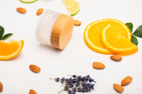 Naranja en rodajas, almendras, flores de lavanda y recipiente con crema casera en la superficie blanca - foto de stock