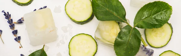 Draufsicht auf frische Gurkenscheiben in der Nähe von Eiswürfeln und Lavendelblüten auf weiß, Banner — Stockfoto