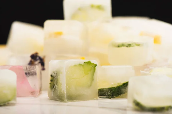 Vista de cerca de la pila borrosa de cubitos de hielo de frutas y verduras en la superficie blanca aislada en negro - foto de stock