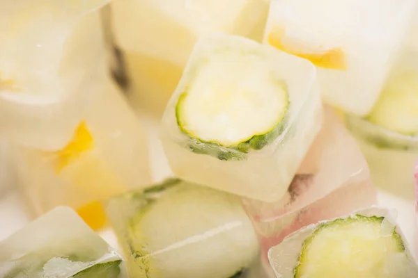 Vista de cerca de refrescantes cubitos de hielo de verduras y frutas sobre fondo blanco borroso - foto de stock