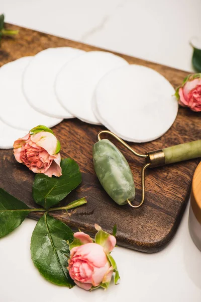 Planche à découper avec rouleau en jade, tampons en coton et roses à thé sur fond de marbre blanc — Photo de stock