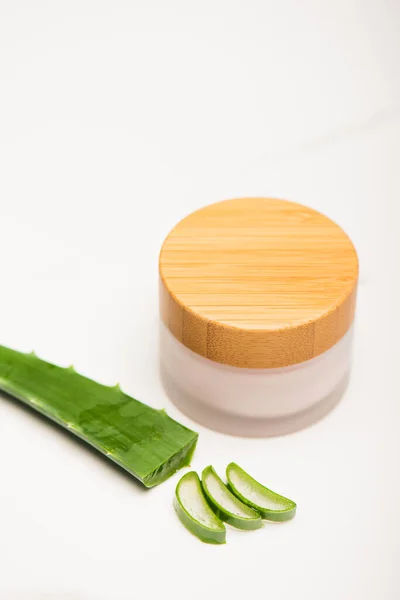 Cut leaf of aloe vera near homemade moisturizing cream on white surface — Stock Photo