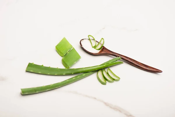 Feuilles d'aloe vera près des tranches, et cuillère en bois avec crème cosmétique maison sur blanc — Photo de stock