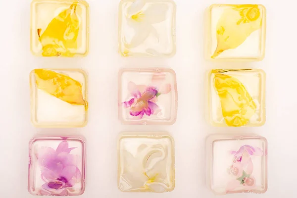 Cubos de hielo congelados florales y frutales transparentes en superficie blanca - foto de stock