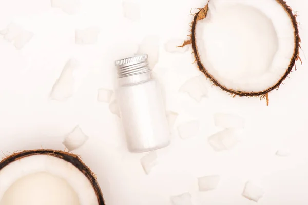 Top view of coconut halves and flakes near bottle with homemade lotion on white — Stock Photo