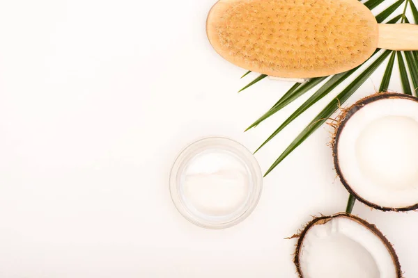 Top view of massage brush, cosmetic cream and coconut halves on white with copy space — Stock Photo