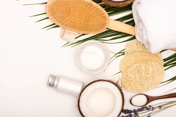Vista dall'alto di spugne, spazzola da massaggio, crema cosmetica, lozione e asciugamano vicino a foglie di palma su bianco — Foto stock