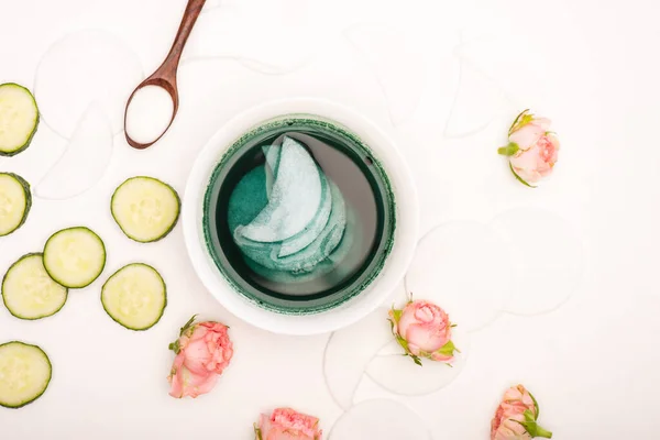 Top view of bowl with tonic and cotton pads, tea roses, fresh cucumber slices and spoon with cosmetic cream on white — Stock Photo