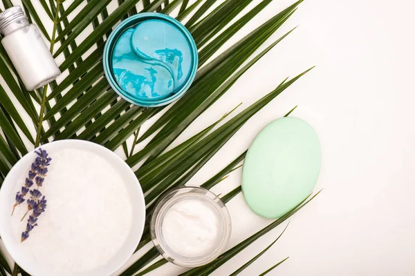 Top view of bowl with lavender, cosmetic cream, scrub, and soap near palm leaves on white — Stock Photo