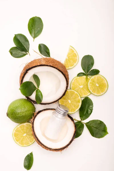 Draufsicht auf Limetten, Kokosnusshälften, eine Flasche Lotion und Rosenblätter auf Weiß — Stockfoto