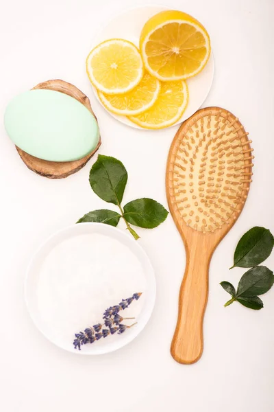 Vista dall'alto di spazzola, ciotola con lavanda, limone a fette, sapone e foglie di rosa su bianco — Foto stock