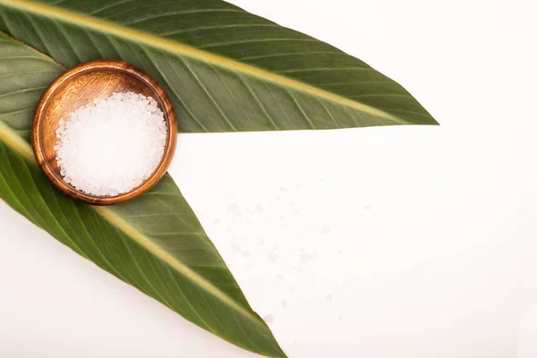 Top view of wooden bowl with sea salt and green leaves on white surface — Stock Photo