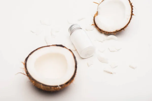Бутылка самодельного лосьона рядом с кокосовыми половинками и хлопьями на белой поверхности — стоковое фото
