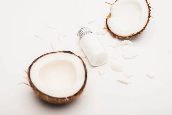 Flasche hausgemachte Lotion in der Nähe von Kokosnusshälften und Flocken auf weißer Oberfläche — Stockfoto