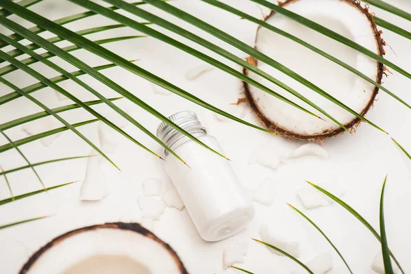 Coconut halves, flakes and homemade lotion under palm leaves on white surface — Stock Photo