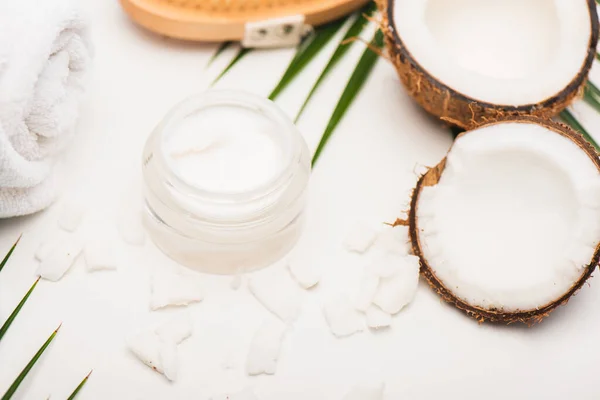 Moitiés de noix de coco, flocons, récipient avec crème cosmétique et serviette sur fond blanc — Photo de stock
