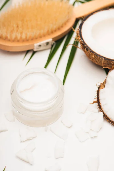 Coconut halves and flakes near homemade cosmetic cream and massage brush on blurred background — Stock Photo