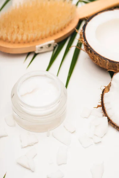 Cocco metà e fiocchi vicino crema cosmetica fatta in casa e spazzola da massaggio su sfondo sfocato — Foto stock