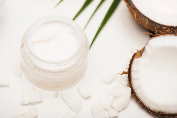 Container with homemade cream near palm leaves, coconut halves and flakes on white — Stock Photo