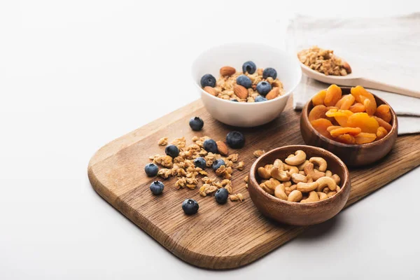 Deliciosa granola com nozes, damascos secos e mirtilo em tábua de madeira sobre fundo branco — Fotografia de Stock