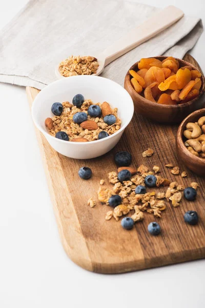 Deliciosa granola com nozes, damascos secos e mirtilo em tábua de madeira sobre fundo branco — Fotografia de Stock