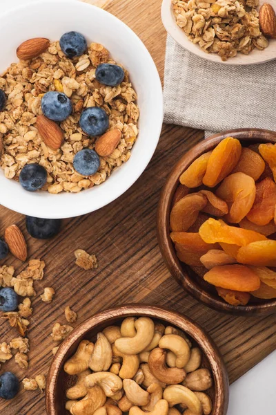 Blick von oben auf köstliches Müsli mit Nüssen, Blaubeeren und getrockneten Aprikosen auf Holzbrett — Stockfoto