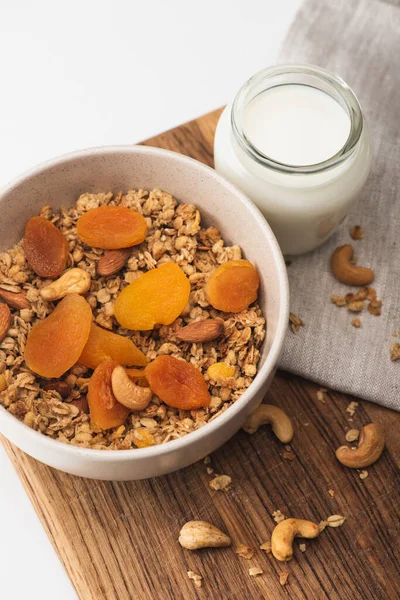 Вид сверху на вкусную гранолу с орехами, сушеными абрикосами и йогуртом на деревянной доске на белом фоне — стоковое фото