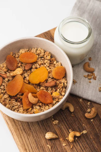 Blick von oben auf köstliches Müsli mit Nüssen, getrockneten Aprikosen und Joghurt auf Holzbrett auf weißem Hintergrund — Stockfoto