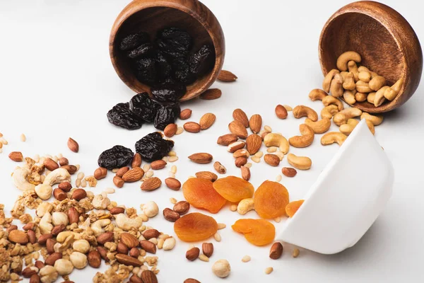 Delicious granola with nuts and dried fruits scattered from bowls on white — Stock Photo