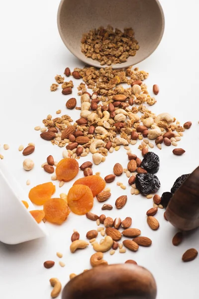 Köstliches Müsli mit Nüssen und getrockneten Früchten aus Schüsseln auf weiß verstreut — Stockfoto