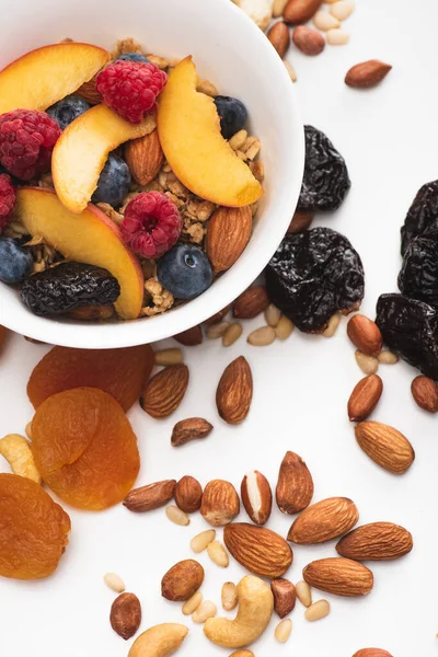 Delicious granola with nuts, berries and fruits in bowl on white — Stock Photo