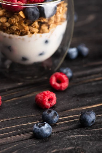 Крупним планом смачна гранола з ягодами та йогуртом у скляній чашці на дерев'яній поверхні — стокове фото