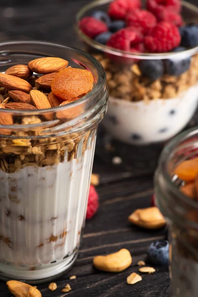 Nahaufnahme von köstlichem Müsli mit getrockneten Aprikosen, Nüssen und Joghurt in Glasbecher auf verschwommenem Hintergrund — Stockfoto