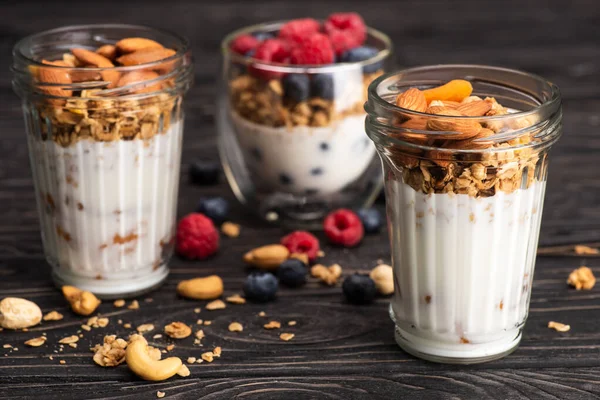 Deliciosa granola con albaricoques secos, nueces y yogur en copas de vidrio sobre superficie de madera sobre fondo borroso - foto de stock