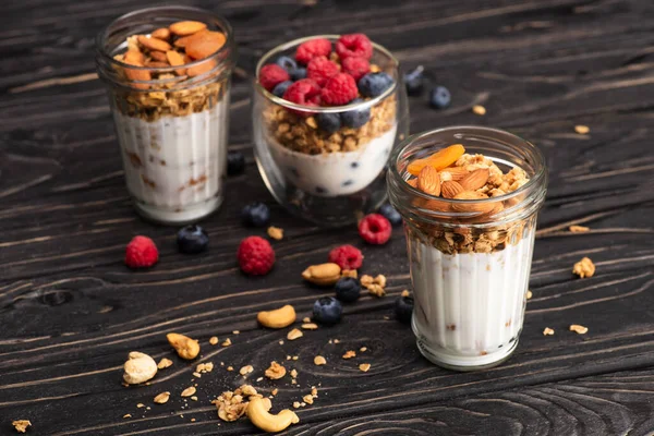 Delicious granola with dried apricots, nuts and yogurt in glass cups on wooden surface on blurred background — Stock Photo