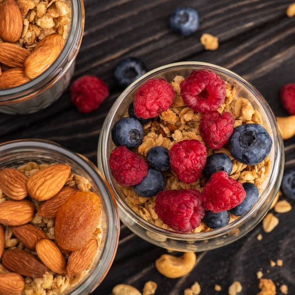 Closeup of delicious granola with berries, dried apricots, nuts and yogurt in glass cups on wooden surface — Stock Photo